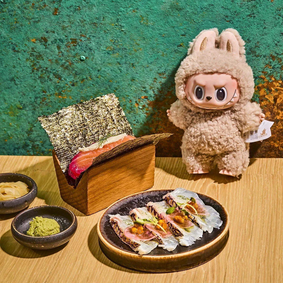 A Labubu beside a salmon gravlax handroll and madai sashimi at Mai